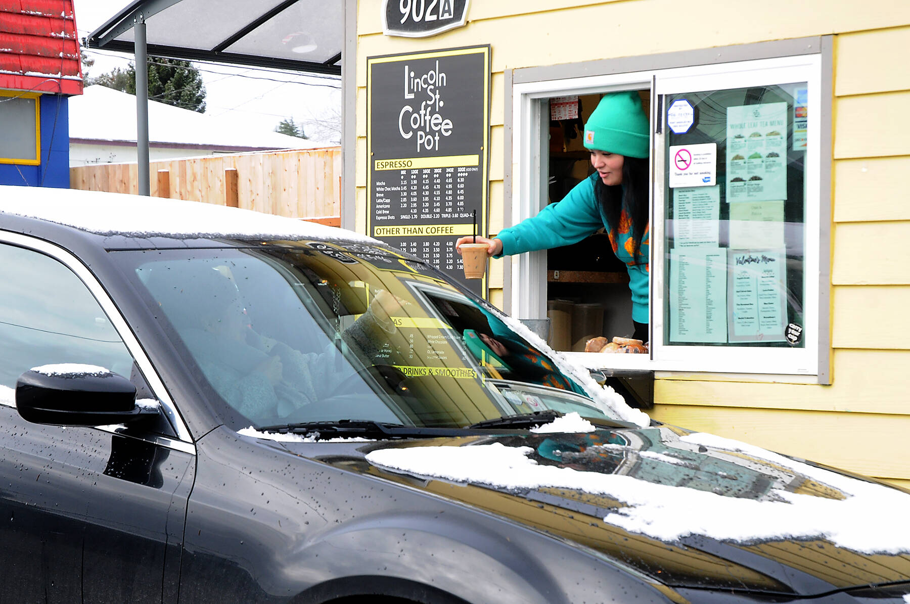 Andie Spencer, a barista at the Lincoln Street Coffee Pot in Port Angeles, hands a drink order to a customer in a snow-covered car on Wednesday after the city received a dusting of snow overnight at sea level. Higher elevations reported up to 2 inches of snow. Areas across the North Olympic Peninsula, including in Forks and Port Townsend, received little snow overnight. Scattered periods of snow with cold temperatures are expected into early next week across the Peninsula. (Keith Thorpe/Peninsula Daily News)