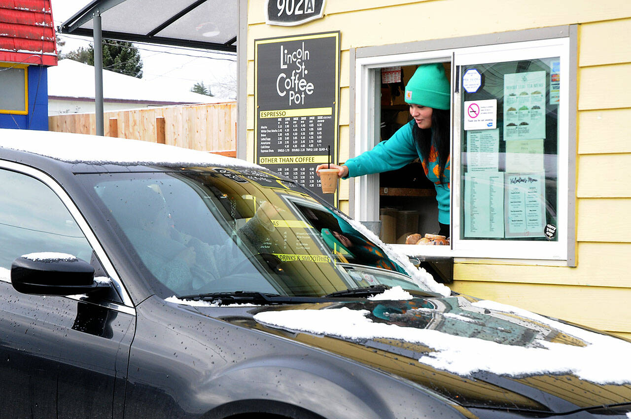 Keith Thorpe / Peninsula Daily News
Andie Spencer, a barista at the Lincoln Street Coffee Pot in Port Angeles, hands a drink order to a customer in a snow-covered car on Wednesday after the city received a dusting of snow overnight at sea level. Higher elevations reported up to 2 inches of snow. Areas across the North Olympic Peninsula, including in Forks and Port Townsend, received little snow overnight. Scattered periods of snow with cold temperatures are expected into early next week across the Peninsula.