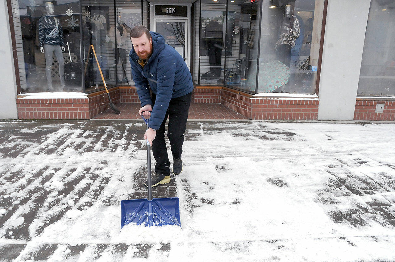 Eric Brown, owner of Browns Outdoor in downtown Port Angeles, scrapes away a layer of ice and snow from the sidewalk in front of the business on Thursday morning. (Keith Thorpe/Peninsula Daily News)