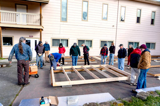 Retired contractor Dave Merrill of Sequim uses a nail gun Wednesday to demonstrate the proper and safe nailing technique to a group of 14 Community Build volunteers who will soon build 10 tiny homes on property owned by New Life Church in Port Townsend. The houses will go to the Caswell-Brown Village managed by Olympic Community Action Programs. (Steve Mullensky/for Peninsula Daily News)