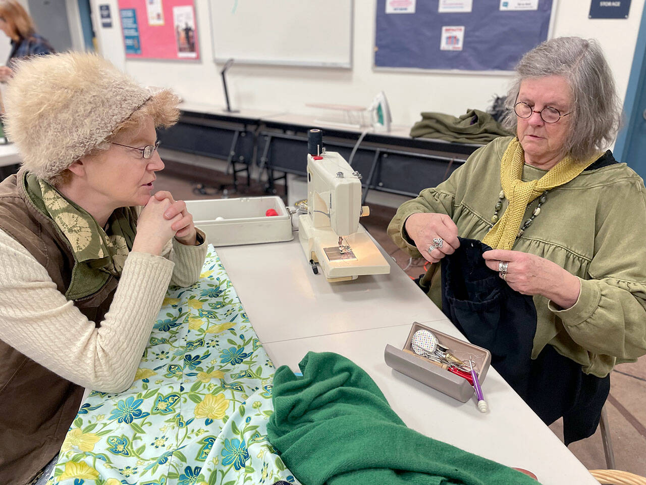 Loran Scruggs, left, brought a green cashmere sweater, a pair of floral silk pants and a pair of black cotton pants that needed to be mended to the Port Townsend Marine Science Center’s Repair Cafe. Paula Lalish was one of three volunteers on hand to assist people by fixing clothing that had holes, rips, tears and and broken zippers. (Paula Hunt/Peninsula Daily News)