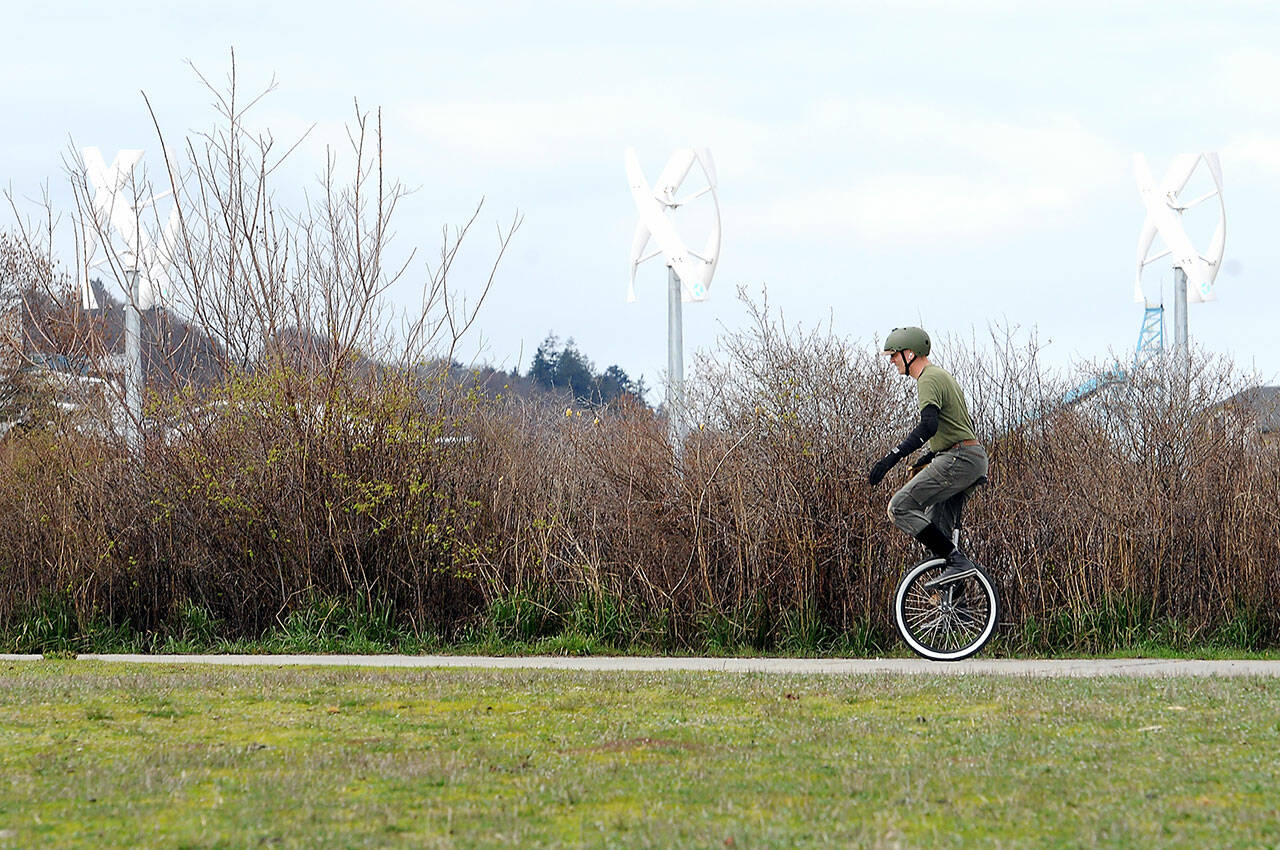 Christian Hoy of Port Angeles practices riding his new unicycle against a backdrop of wind turbine spires at Pebble Beach Park on the Port Angeles waterfront on Tuesday. (KEITH THORPE/PENINSULA DAILY NEWS)