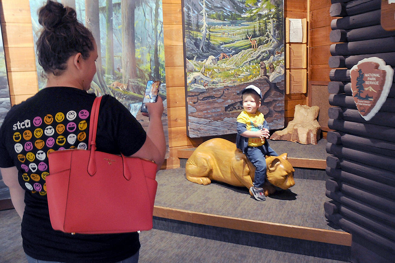 Savanna Hoglund of Spokane takes a photo of her son, Lincoln Hoglund, 2, as hit sits on a wooden cougar sculpture in the Discovery Room on Tuesday at the Olympic National Park Visitor Center in Port Angeles. The center features a variety of displays that provide a sampling of what can be found within the park, as well as interactive exhibits for children. (Keith Thorpe/Peninsula Daily News)
