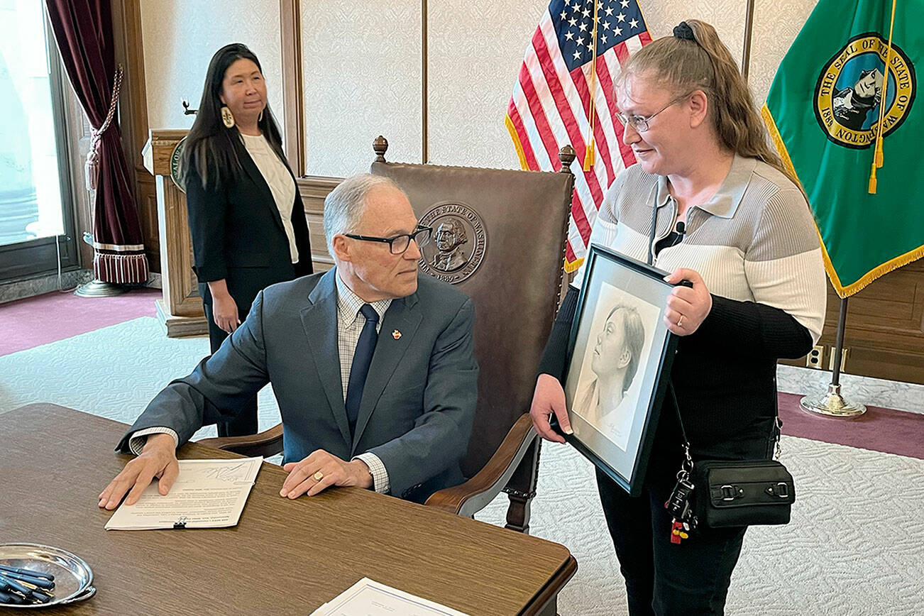 Dawn Reid, right, shows Gov. Jay Inslee a pencil drawing of her daughter, Kimberly, after Inslee signed a bill titled with Kimberly’s name. State Rep. Debra Lekanoff, left, took part in the ceremony. (Gabe Galanda)