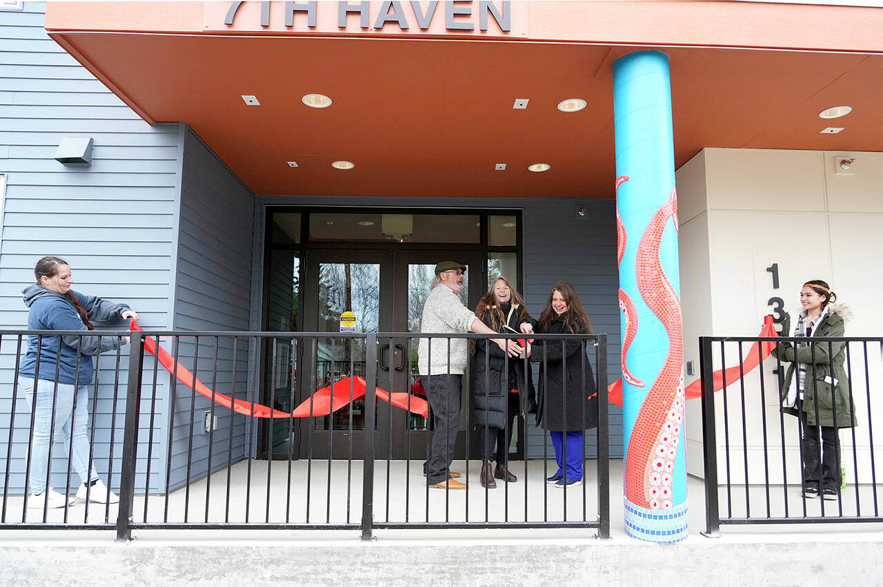 Dale Wilson, past executive director of Olympic Comunity Action Programs, and Cherish Cronmiler, current executive director, cut the ceremonial ribbon officially opening the 43-unit low cost housing units. (Steve Mullensky/for Peninsula Daily News)