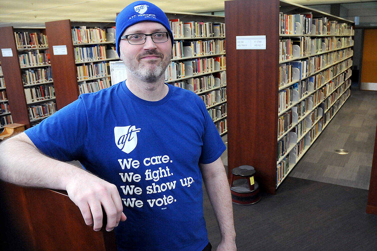 Tim Williams, instructional and reference librarian at Peninsula College and president of the college’s Faculty Association, displays his American Federation of Teachers shirt and hat on Tuesday on the Port Angeles campus. He said that while Peninsula College faculty were not participating in a community college walkout planned in Seattle, Olympia, Lynnwood and Tacoma, they are supporting its aims to pressure the state Legislature into providing more support for community colleges. (Keith Thorpe/Peninsula Daily News)