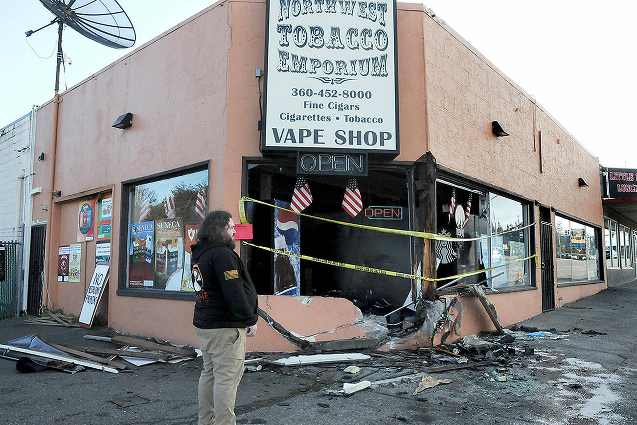Justin Brophy, general manager of Northwest Tobacco Emporium, at 309 E. First St. in Port Angeles, examines the front of the establishment on Wednesday morning after a car crashed into the building and caught fire late Tuesday night. (Keith Thorpe/Peninsula Daily News)