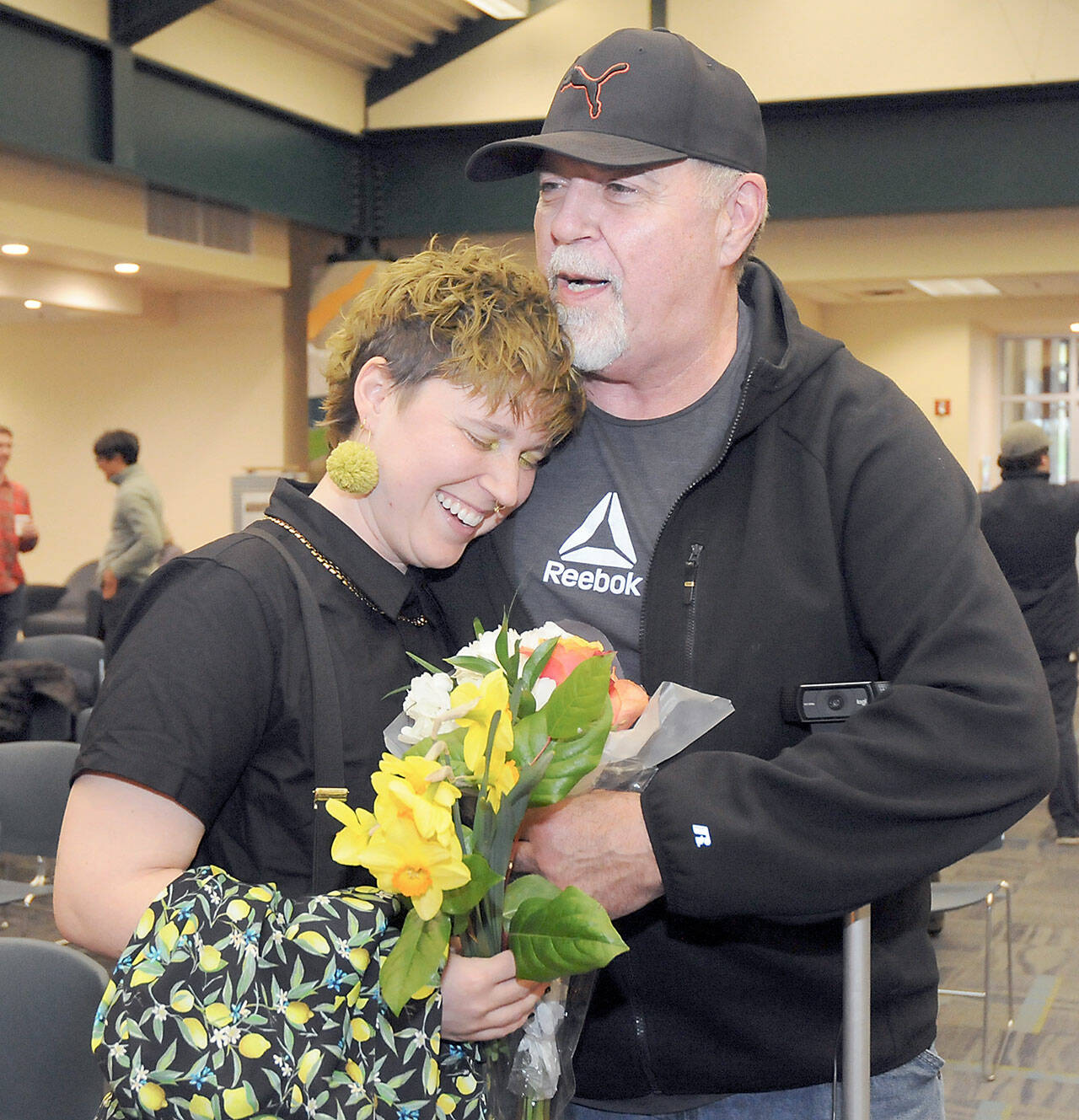 Jaiden Dokken, Clallam County’s first poet laureate, receives a hug and flowers from their father Mark Dokken of Port Angeles after Jaiden was inaugurated to their two-year post on Tuesday at the Port Angeles Public Library. (Keith Thorpe/Peninsula Daily News)