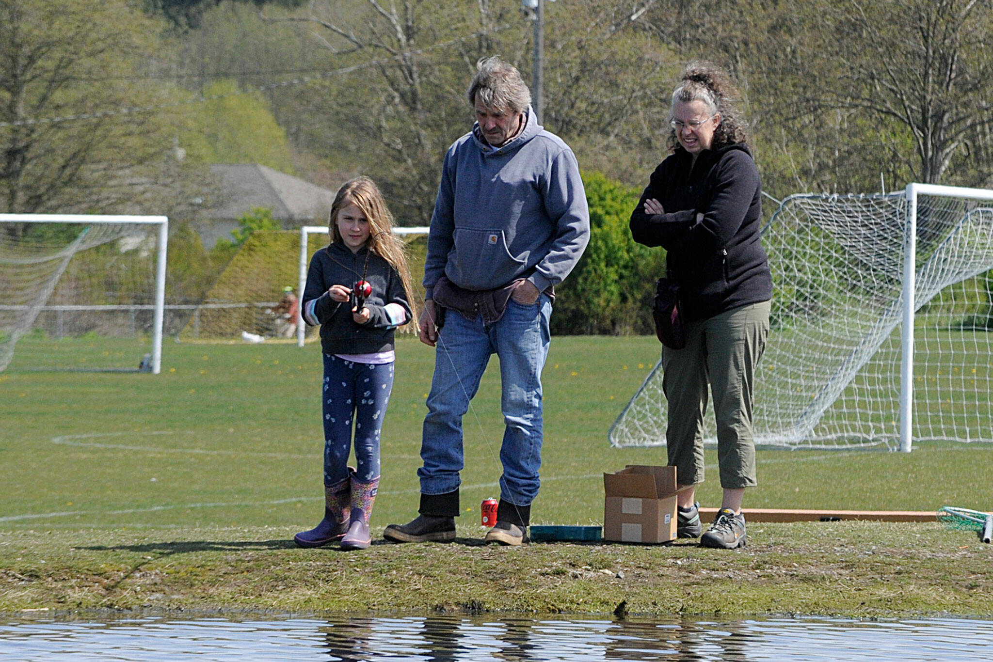 Brooke Pederson, 9, of Joyce reels as parents Erik and Paula watch. She soon caught her first fish during the 2022 Kids Fishing Day. (Matthew Nash/Olympic Peninsula News Group)