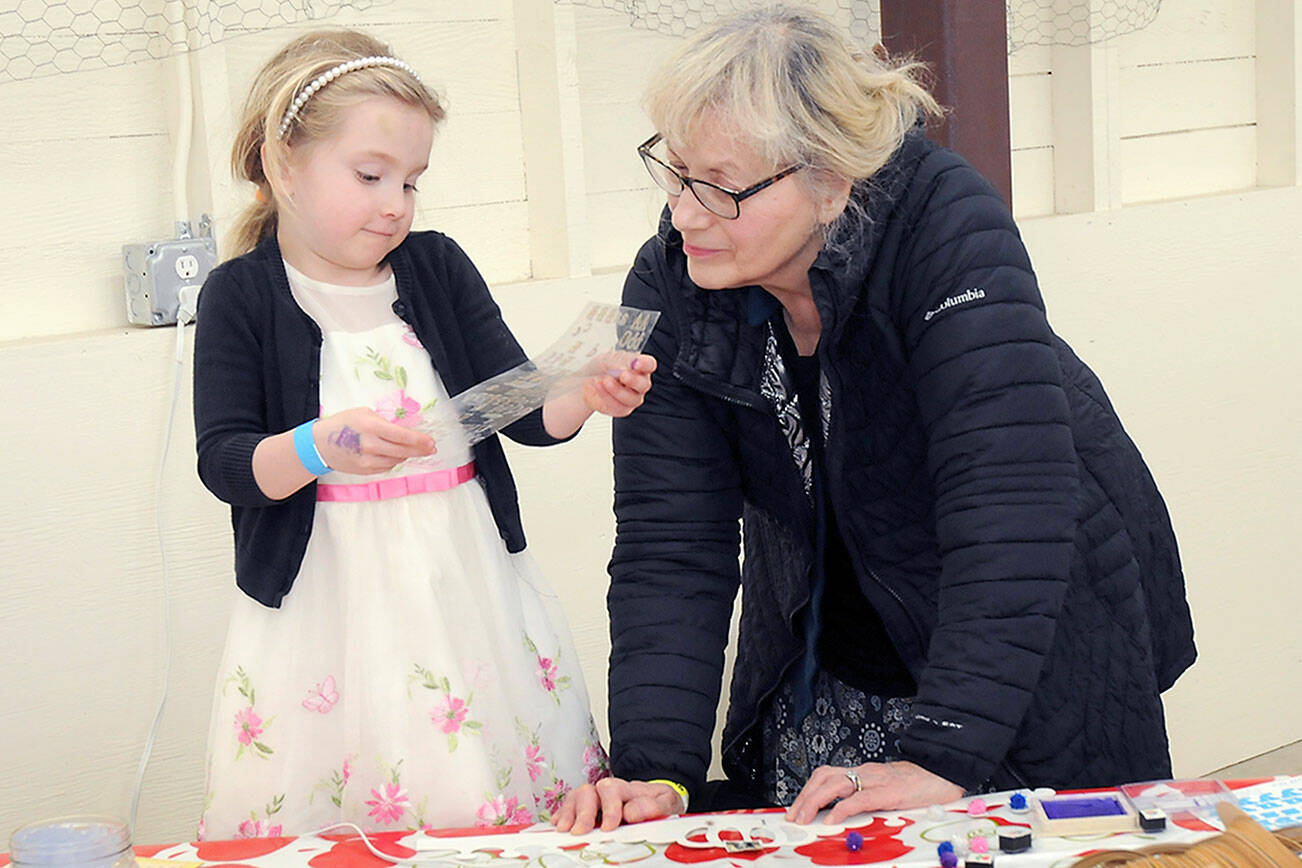Ida Shantz, 5, of Port Angeles looks over a sheet of stenciled letters with her grandmother, Patricia Kessler of Woodburn, Ore., at a cardboard crown craft table during Saturday’s Barn Dance at the Clallam County Fairgrounds to benefit the Five Acre School north of Sequim. The dance also included food, entertainment, children’s activities and a silent auction. (Keith Thorpe/Peninsula Daily News)
