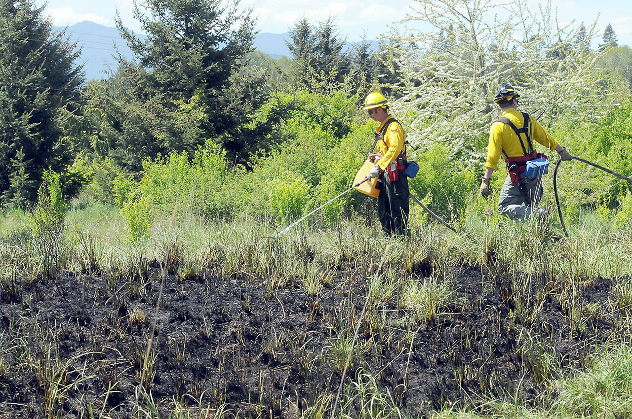 Clallam County Fire District 2 firefighters Chris Dalen, left and Zach Gear put out hot spots around the perimeter of a brush fire near 2333 Lower Elwha Road on Friday. The fire burned an area approximately 200 feet by 200 feet while scorching a tree and threatening a nearby mobile home. (KEITH THORPE/PENINSULA DAILY NEWS)