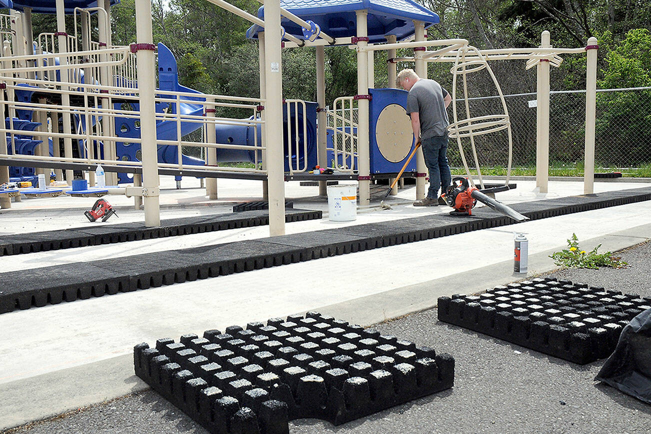 KEITH THORPE/PENINSULA DAILY NEWS
Riley Peterson of R & R Construction of Carbonado applies adhesive to the concrete base surrounding the playground equipment at Shane Park on Tuesday in Port Angeles in preparation for the replacement of cushioned tiles that make up the play surface. The rubberized tiles began to become loose in 2022 due to shrinkage and weather, forcing the playground's closure in September of that year.  The project, which will use as many of the original tiles as can be salvaged intermixed with new replacement tiles and new adhesive, is expected to be completed by mid-June.