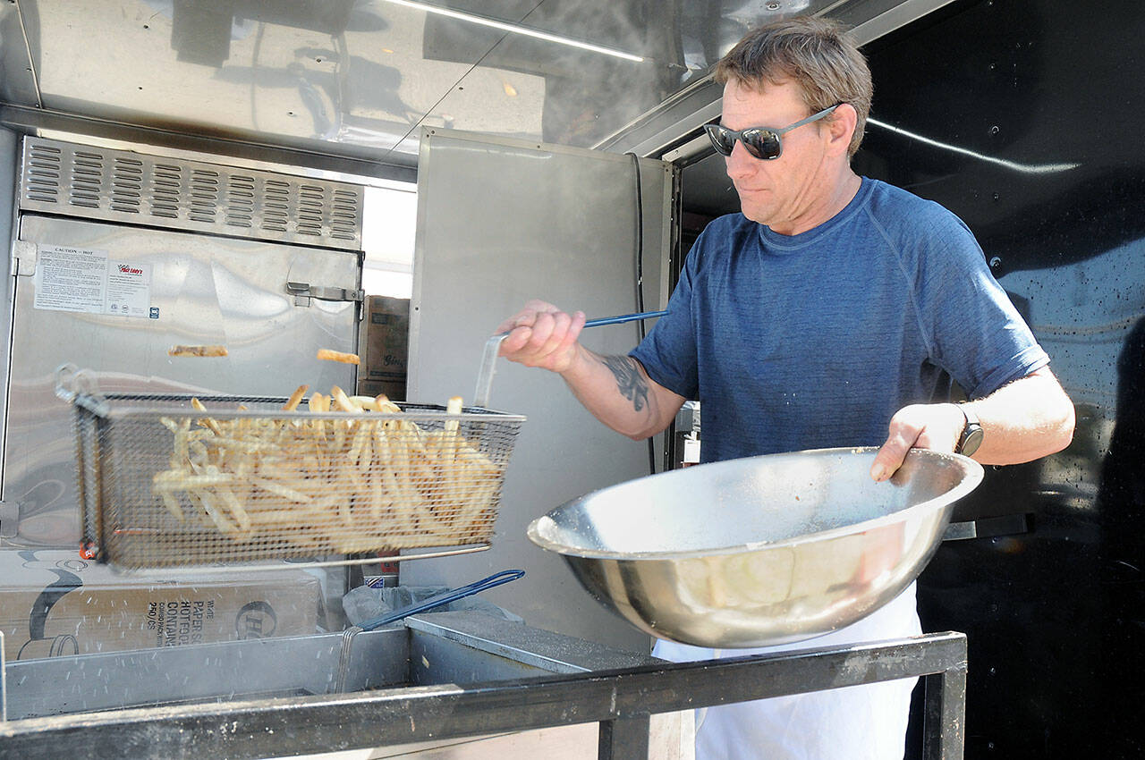 Brian Jennings, general manager and cook at the Coyote BBQ and Kokopelli Grill catering truck, shakes a basket of freshly-cooked french fries on Friday at the Juan de Fuca Festival street fair in Port Angeles.