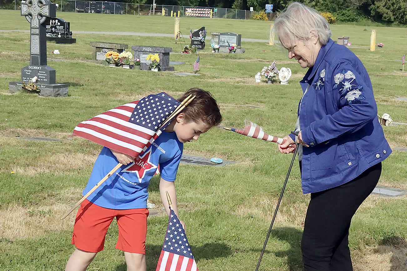 Samuel Jones, 9, and Grace Kauffman help place hundreds of flags on graves of deceased veterans at Ocean View Cemetery early Saturday morning. The tradition this year was led by the Daughters of the American Revolution organization. (Dave Logan/for Peninsula Daily News)