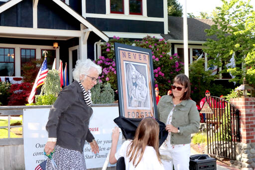 Betsy Schultz, left, and Claire Rausch unveil a painting especially drawn for the Captain Joseph House on Monday. The artwork was done by a Michael Reagan, a veteran who features military men and women who have been lost in the service to their country. This was the 12th Memorial Day ceremony held at Captain Joseph House, at 1108 S. Oak St. in Port Angeles, which is now open to Gold Star families. (Dave Logan/for Peninsula Daily News)