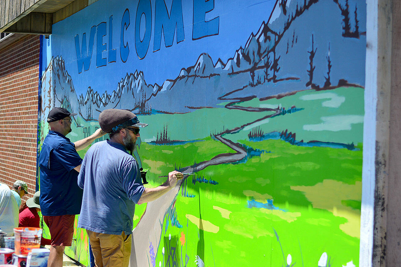 In a PT Artscape project, Blue Heron Middle School teacher Charlie Fornia, left, and artist Jesse Watson finish painting a “Welcome to PTHS” mural on the woodshop building at Port Townsend High School. PT Artscape hired Watson to design the mural and hosted a morning of painting with elementary, middle school and high school students from around Port Townsend. (Diane Urbani de la Paz/for Peninsula Daily News)