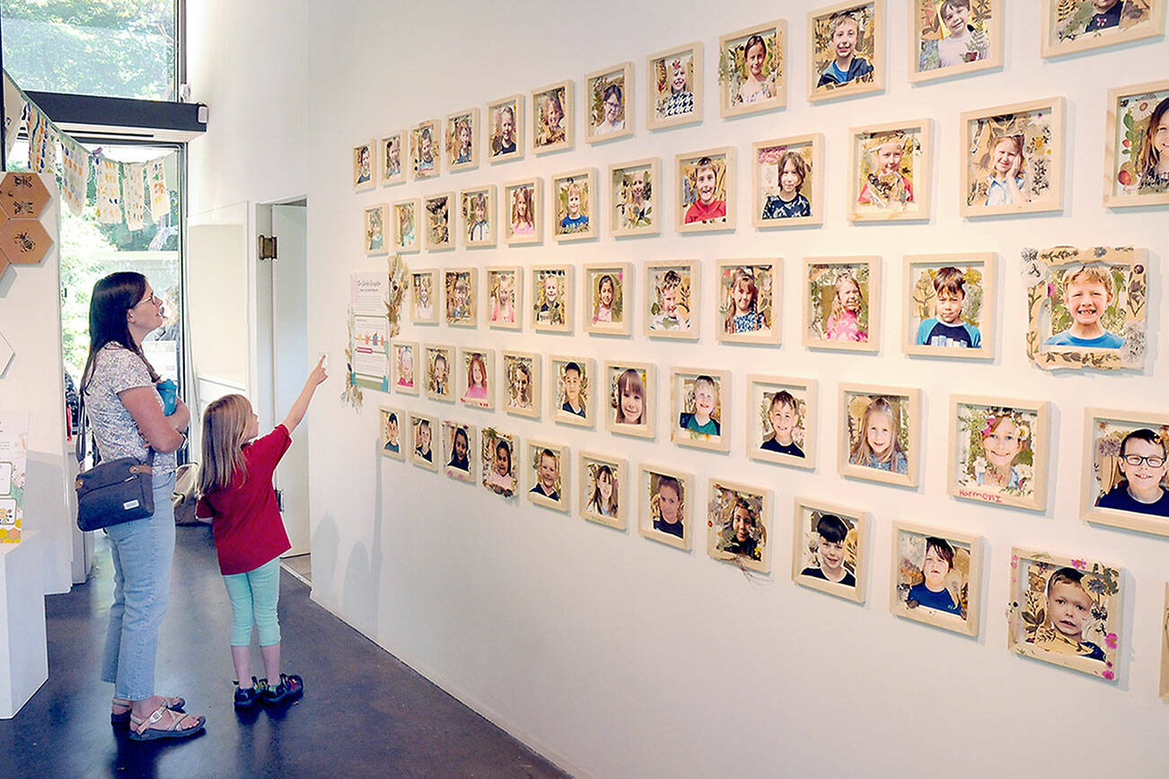 KEITH THORPE/PENINSULA DAILY NEWS
Janel Bistrika of Port Angeles and her daughter, Amelia Bistrika, 7, look at a wall of photographs of first-grade students, including Amelia, who took part in the garden-themed "Blooming Artists" exhibition during an opening reception on Tuesday at the Port Angeles Fine Arts Center. "Blooming Artists" features the works of about 275 youngsters and will run through June 25.