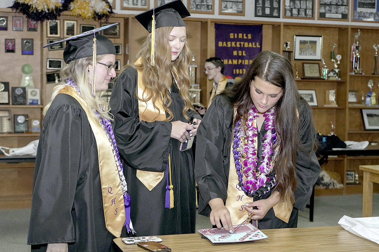 Quilcene High School graduate Rhiannon Chapman, right, puts the finishing touches on her mortar board while Ashley Jones, center, and Zoey Carver, left, watch. The trio were waiting for their graduation ceremony to start on Saturday at the high school. (Steve Mullensky/for Peninsula Daily News)
