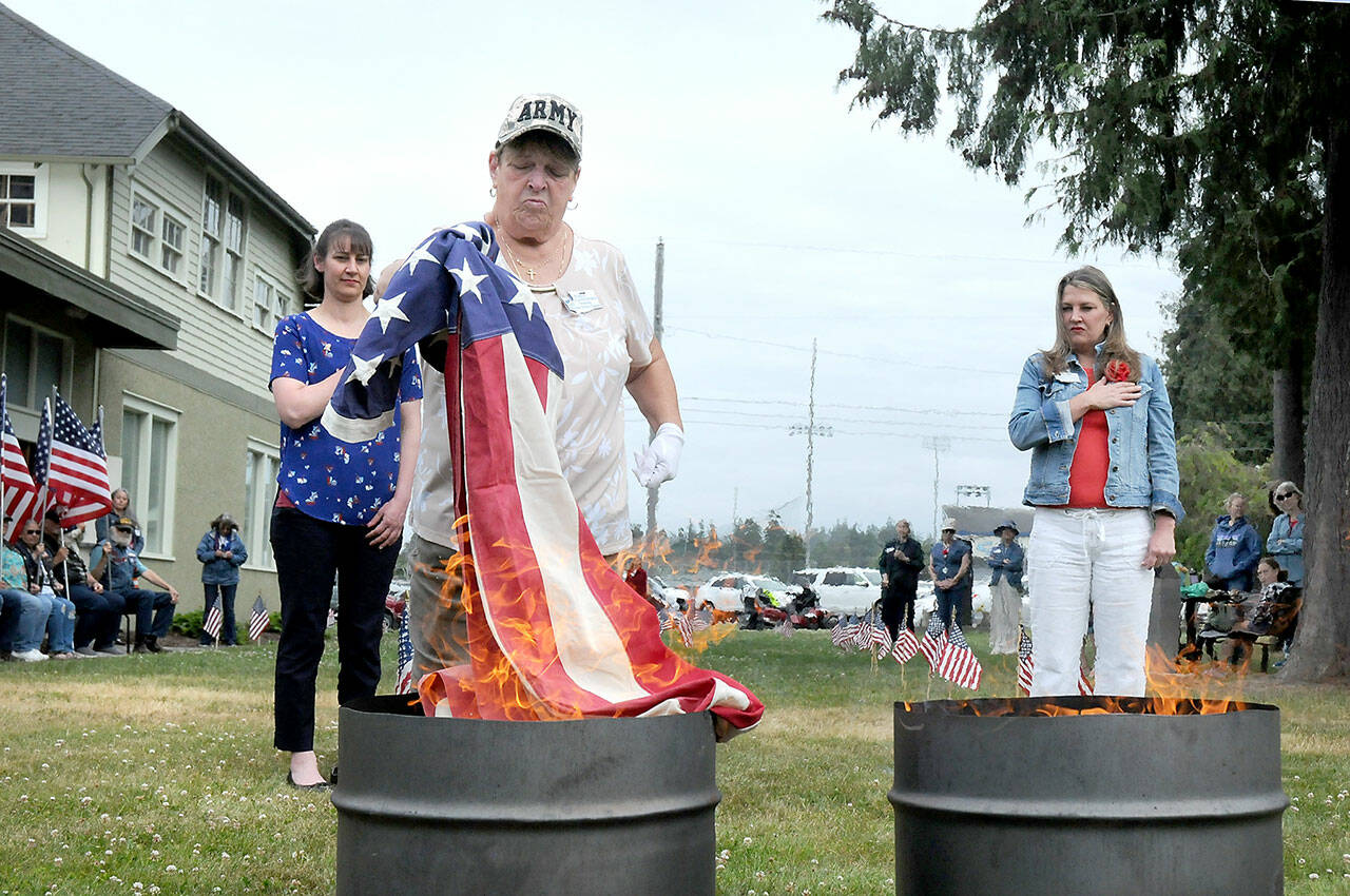 U.S. Army veteran Nancy Zimmerman, a member of the Michael Trebert Chapter of the Daughters of the American Revolution, is flanked by fellow DAR members Amira-Lee Salavati, left, and Lindsey Christianson as Zimmerman incinerates a used American Flag during a flag retirement ceremony on Wednesday at the Northwest Veterans Resource Center in Port Angeles. A total of 24 cotton flags were burned during the Flag Day ceremony. (Keith Thorpe/Peninsula Daily News)