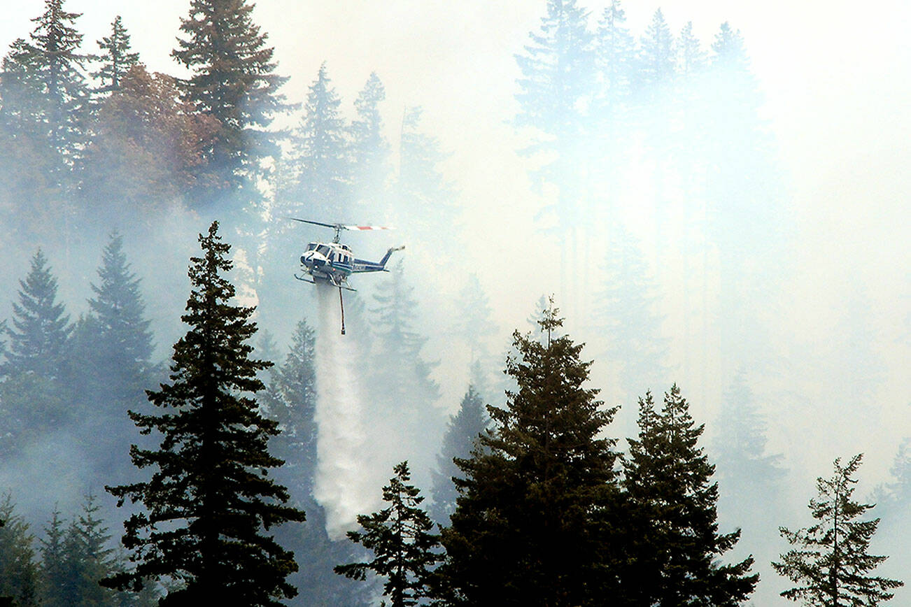 A state Department of Natural Resources helicopter flies through clouds of smoke to dump water on a hotspot of a wildland fire in the Indian Creek Valley on Sunday southwest of Port Angeles. (Keith Thorpe/Peninsula Daily News)