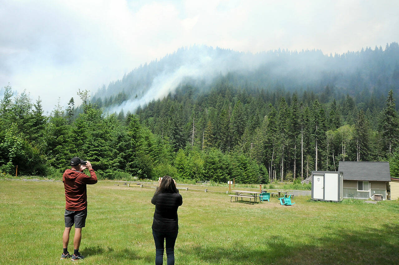 Mark and Jo Bader of Gig Harbor take photos of a smoldering hillside from a clearing behind Granny’s Cafe on U.S Highway 101 in Indian Creek Valley on Sunday. (Keith Thorpe/Peninsula Daily News)