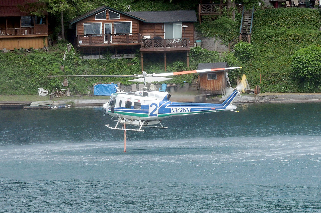 A helicopter operated by the state Department of Natural Resources pumps water from Lake Sutherland to be dumped on a nearby wildland fire on Sunday. (Keith Thorpe/Peninsula Daily News)