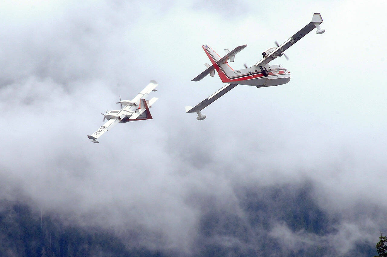 A pair of firefighting aircraft make a banked turn over Lake Crescent after scooping water to fight a nearby wildland fire on Sunday. (Keith Thorpe/Peninsula Daily News)