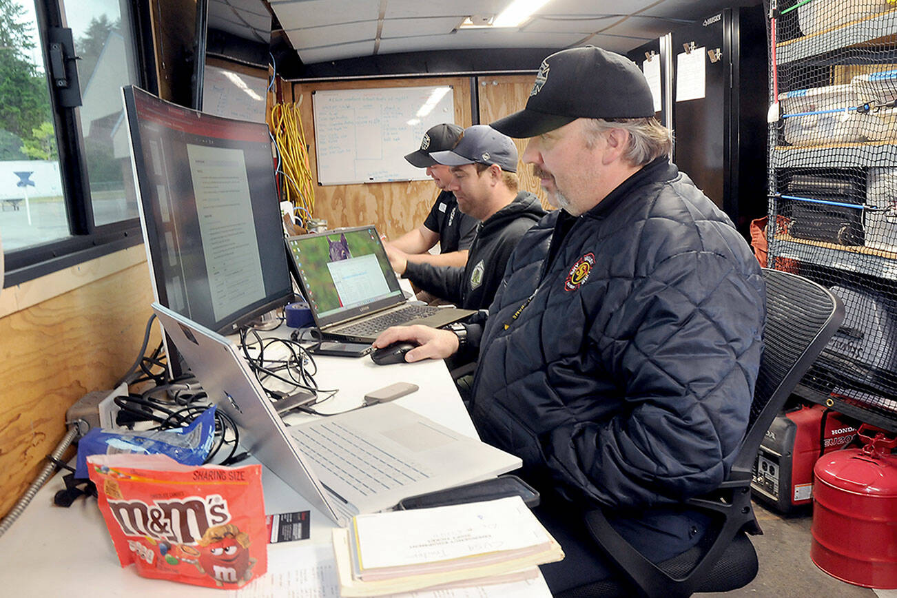 Fire managers, from front, Robert Thurston working with GIS, communications unit leader Carsen Smith and operations section chief Scott Coulson work at a command post for the Lake Sutherland Fire on Tuesday at Dry Creek School in Port Angeles. (Keith Thorpe/Peninsula Daily News)