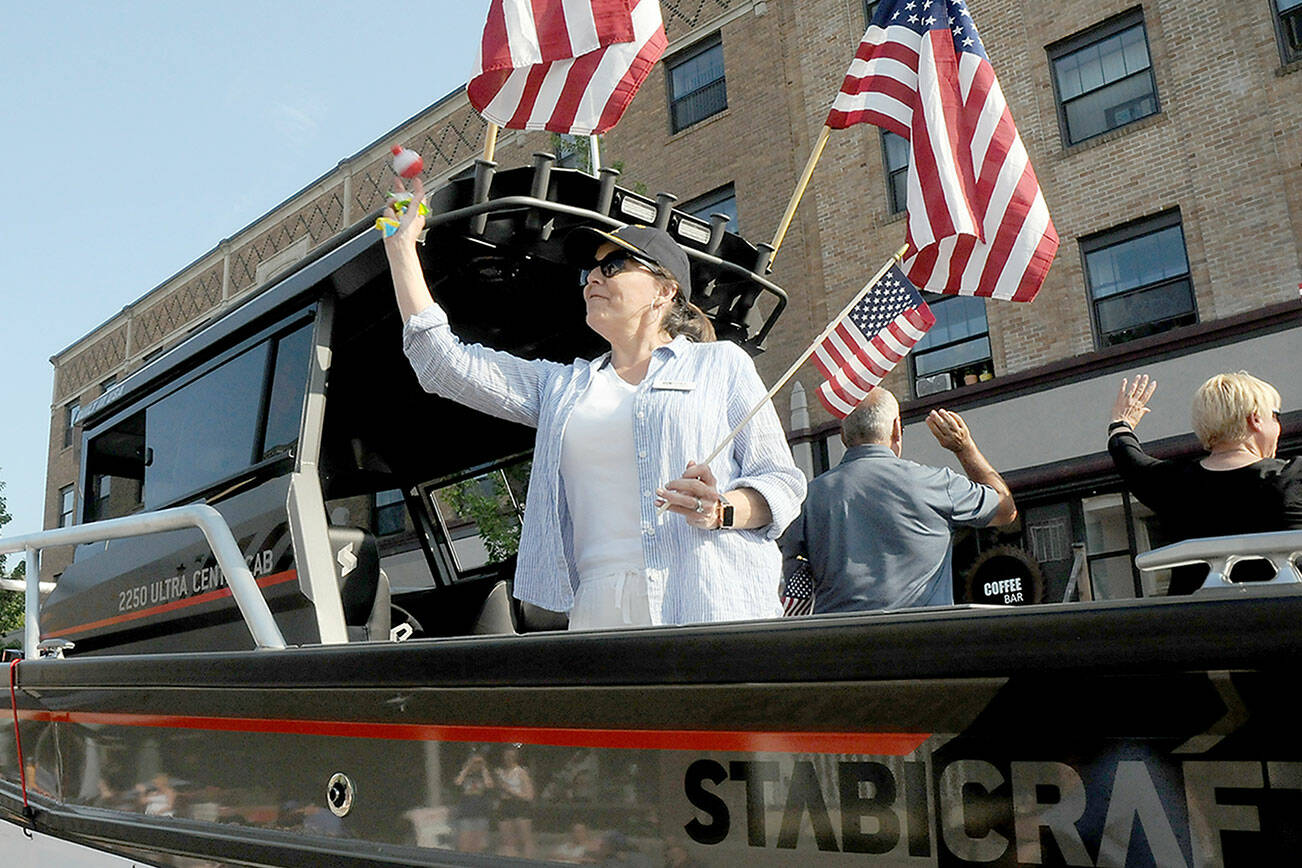 Port of Port Angeles Commissioner Colleen McAleer prepares to toss goodies to the crowd from the back of a trailered boat during Tuesday’s Independence Day parade in Port Angeles. McAleer, along with fellow commissioners Steve Burke and Connie Beauvais, facing the other side, were the parade’s grand marshals in honor of the 100th anniversary of the port. (Keith Thorpe/Peninsula Daily News)