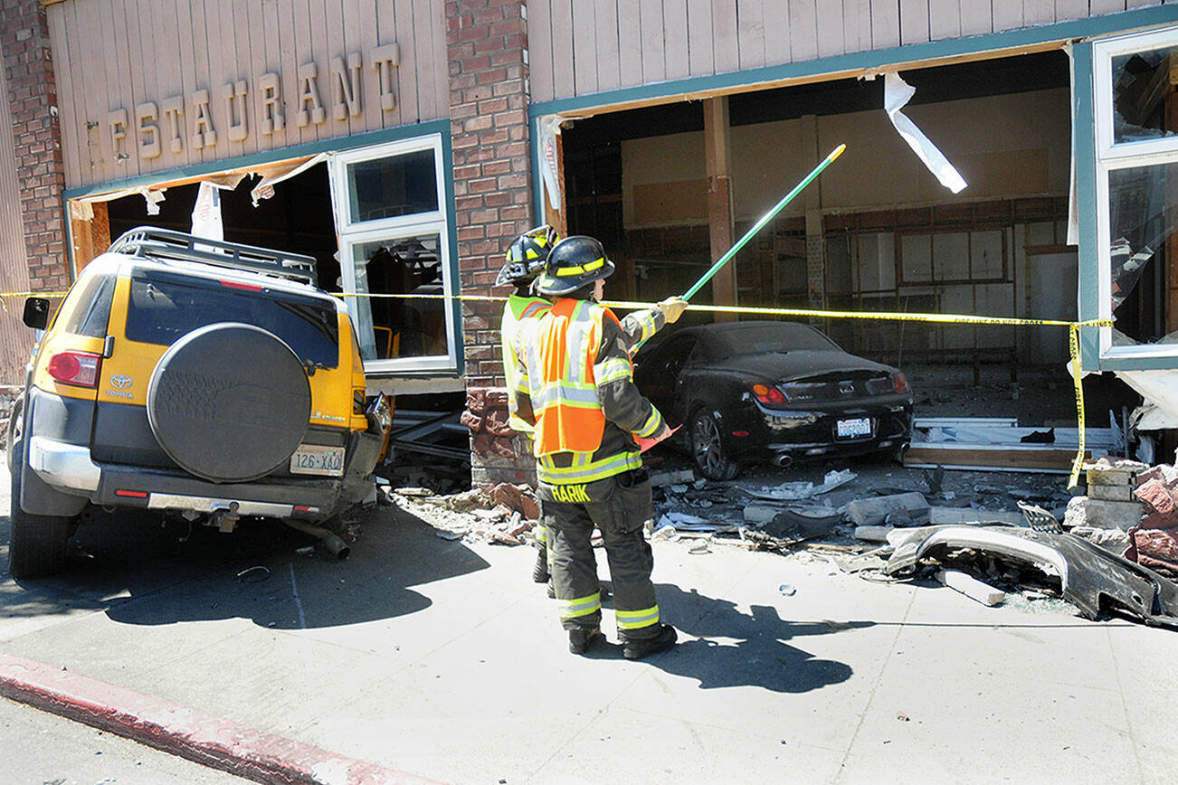 Port Angeles firefighters Ben Clark and Samantha Harik examine a gaping hole in the side of the former Delaney’s Restaurant and Bar at Front and Lincoln streets in downtown Port Angeles after a three-vehicle collision sent two vehicles into the building on Wednesday. (Keith Thorpe/Peninsula Daily News)