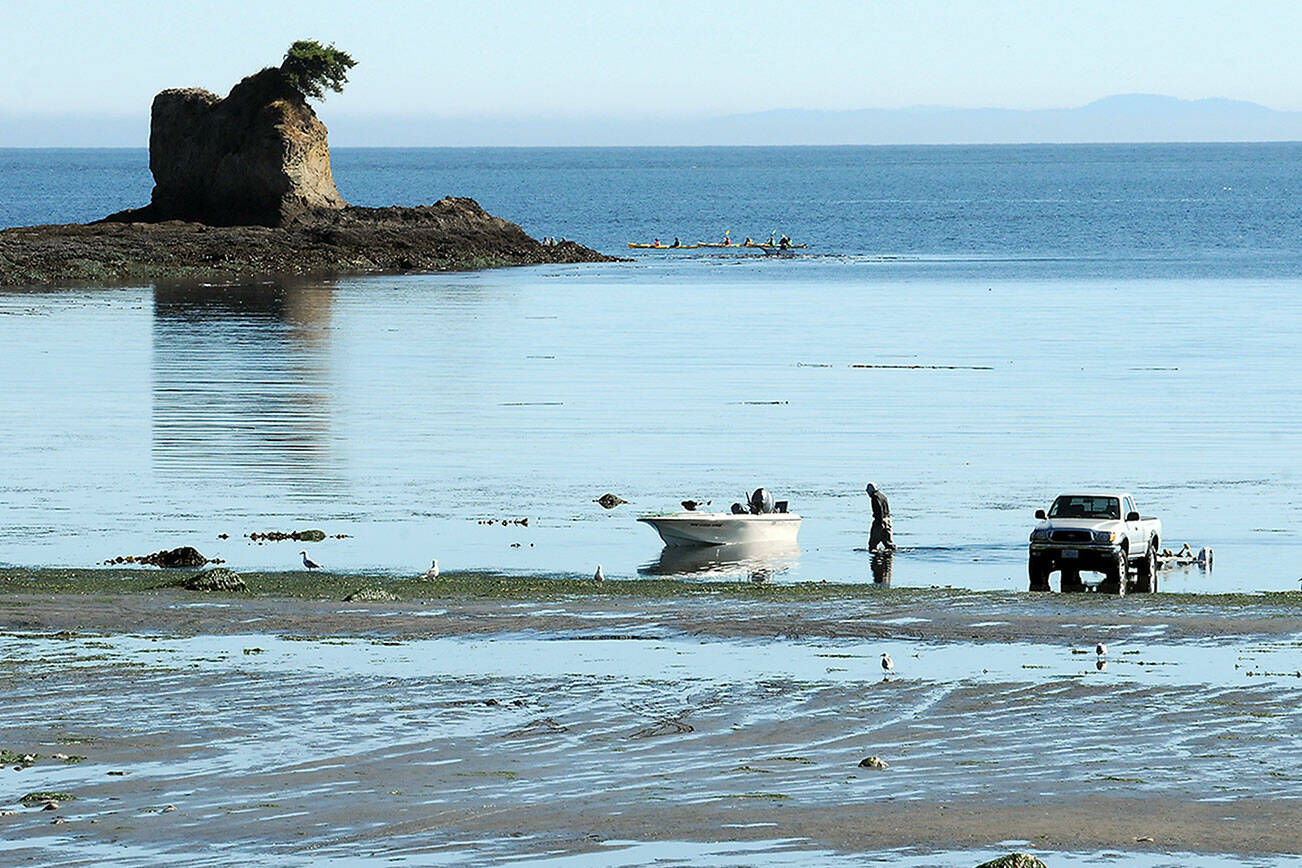 Greg Holmquist of Port Angeles walks to his beached boat to pull it to a waiting trailer, parked more than 100 yards from the end of the regular boat ramp as a group of kayakers paddle around the Bachelor Rock sea stack during Thursday’s minus-2 low tide at Freshwater Bay west of Port Angeles. Holmquist said it was a perfect day for boating with calm seas and pleasant weather. (Keith Thorpe/Peninsula Daily News)