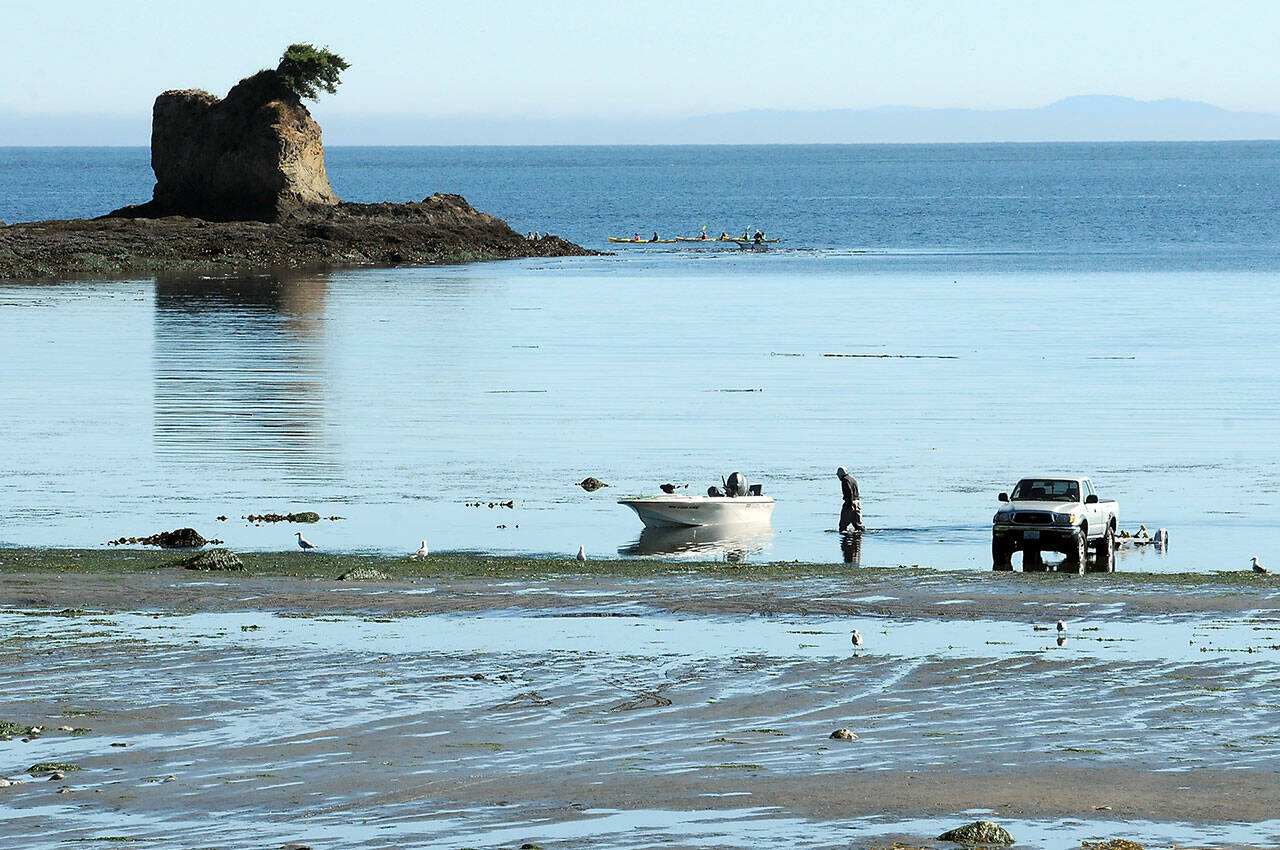 Greg Holmquist of Port Angeles walks to his beached boat to pull it to a waiting trailer, parked more than 100 yards from the end of the regular boat ramp as a group of kayakers paddle around the Bachelor Rock sea stack during Thursdays minus-2 low tide at Freshwater Bay west of Port Angeles. Holmquist said it was a perfect day for boating with calm seas and pleasant weather. (Keith Thorpe/Peninsula Daily News)