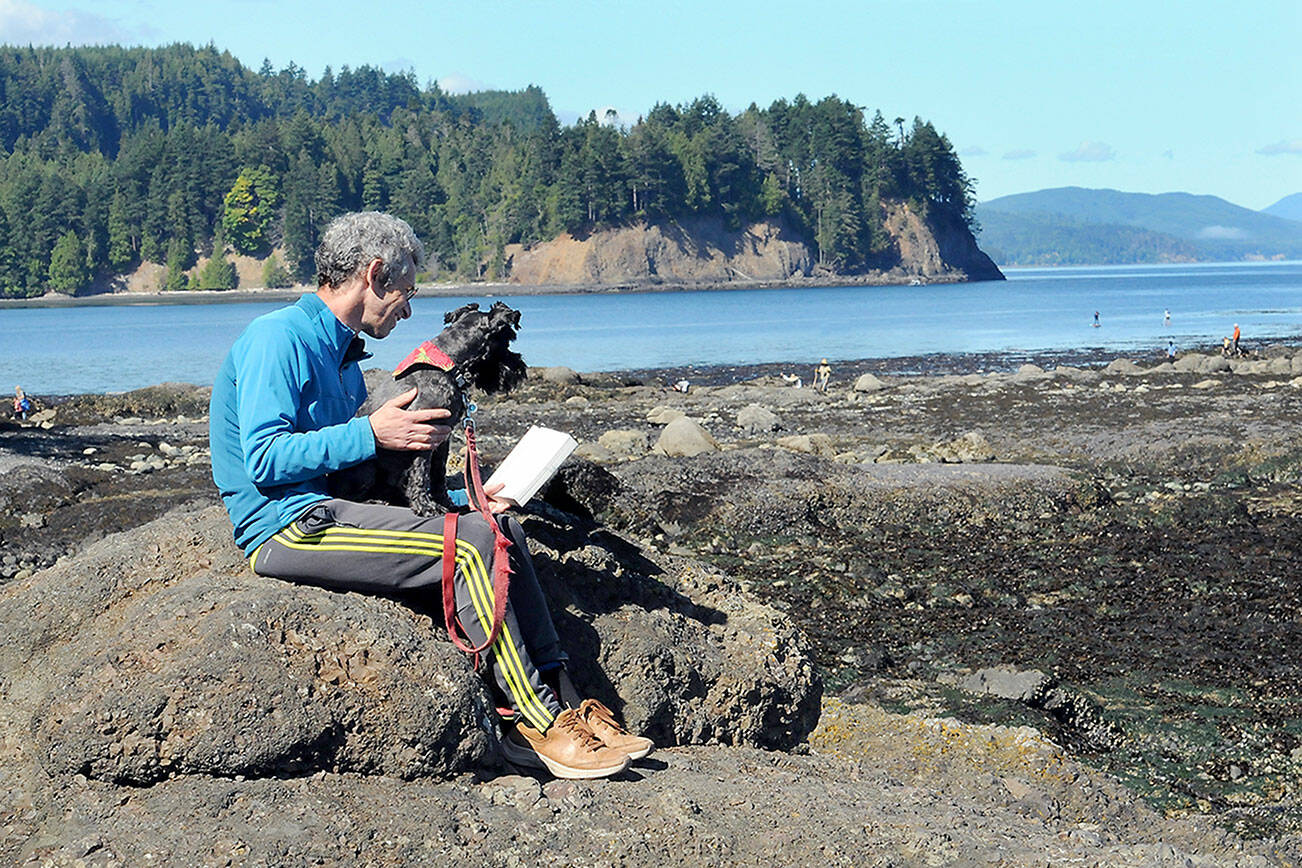 KEITH THORPE/PENINSULA DAILY NEWS
Mike Nossal of Seattle, along with his dog, Pico, reads a book on a rocky outcrop overlooking Tongue Point at the Salt Creek Recreation Area on Thursday north of Joyce. A minus 2 tide revealed large areas of the point, allowing access to the area for tidepool exploration or just enjoying the view.