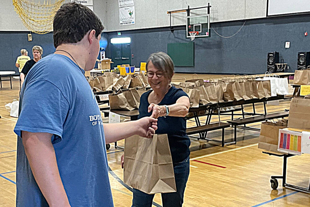 Amala Kuster with the Sequim Sunrise Rotary hands off a bag to James Joseph Dorrell, 14, with the Sequim unit of the Boys & Girls Clubs of the Olympic Peninsula, during the Back to School Fair in 2022. (Matthew Nash/Olympic Peninsula News Group)