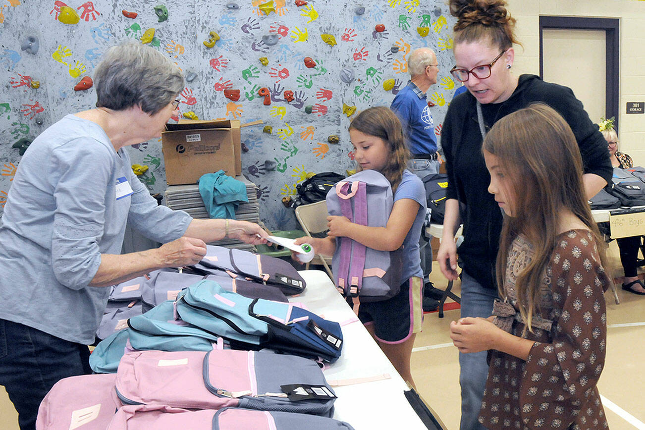 Julia Smith of Port Angeles, center right, oversees her children, fourth-grader Julia Smith, 9, and fifth-grader Shelby Smith, 10, right, pick out backpacks filled with school supplies as volunteer Ann West assists with distribution during Saturday’s back-to-school fair at Jefferson Elementary School in Port Angeles. During the event, students were given free school supplies, with family service opportunities, as well as a lunch, made available at the approach of the 2023-24 school year. (Keith Thorpe/Peninsula Daily News)