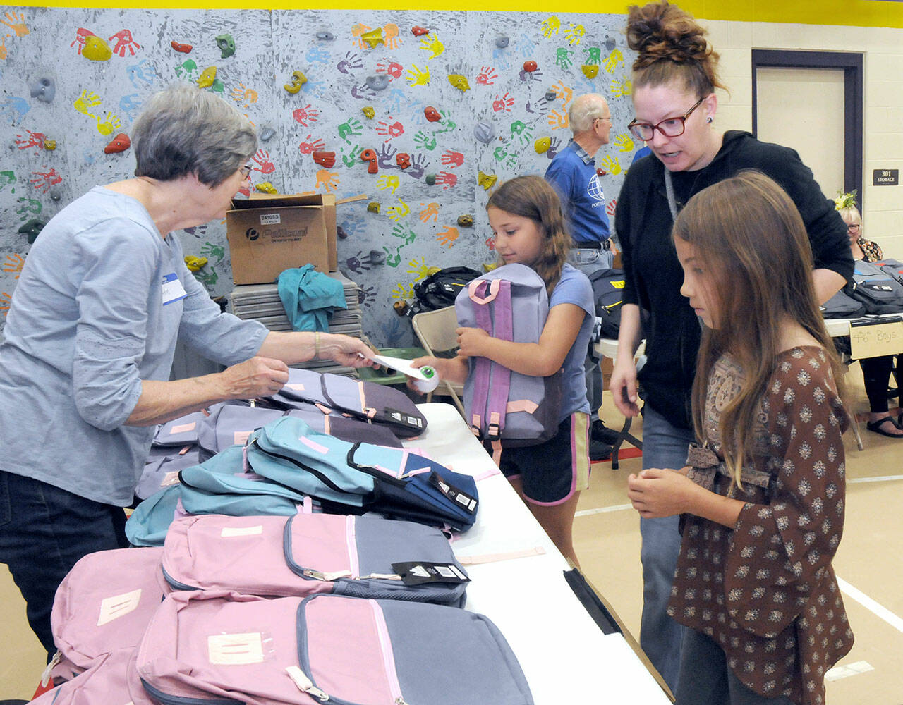 Julia Smith of Port Angeles, center right, oversees her children, fourth-grader Julia Smith, 9, and fifth-grader Shelby Smith, 10, right, pick out backpacks filled with school supplies as volunteer Ann West assists with distribution during Saturdays back-to-school fair at Jefferson Elementary School in Port Angeles. During the event, students were given free school supplies, with family service opportunities, as well as a lunch, made available at the approach of the 2023-24 school year. (Keith Thorpe/Peninsula Daily News)