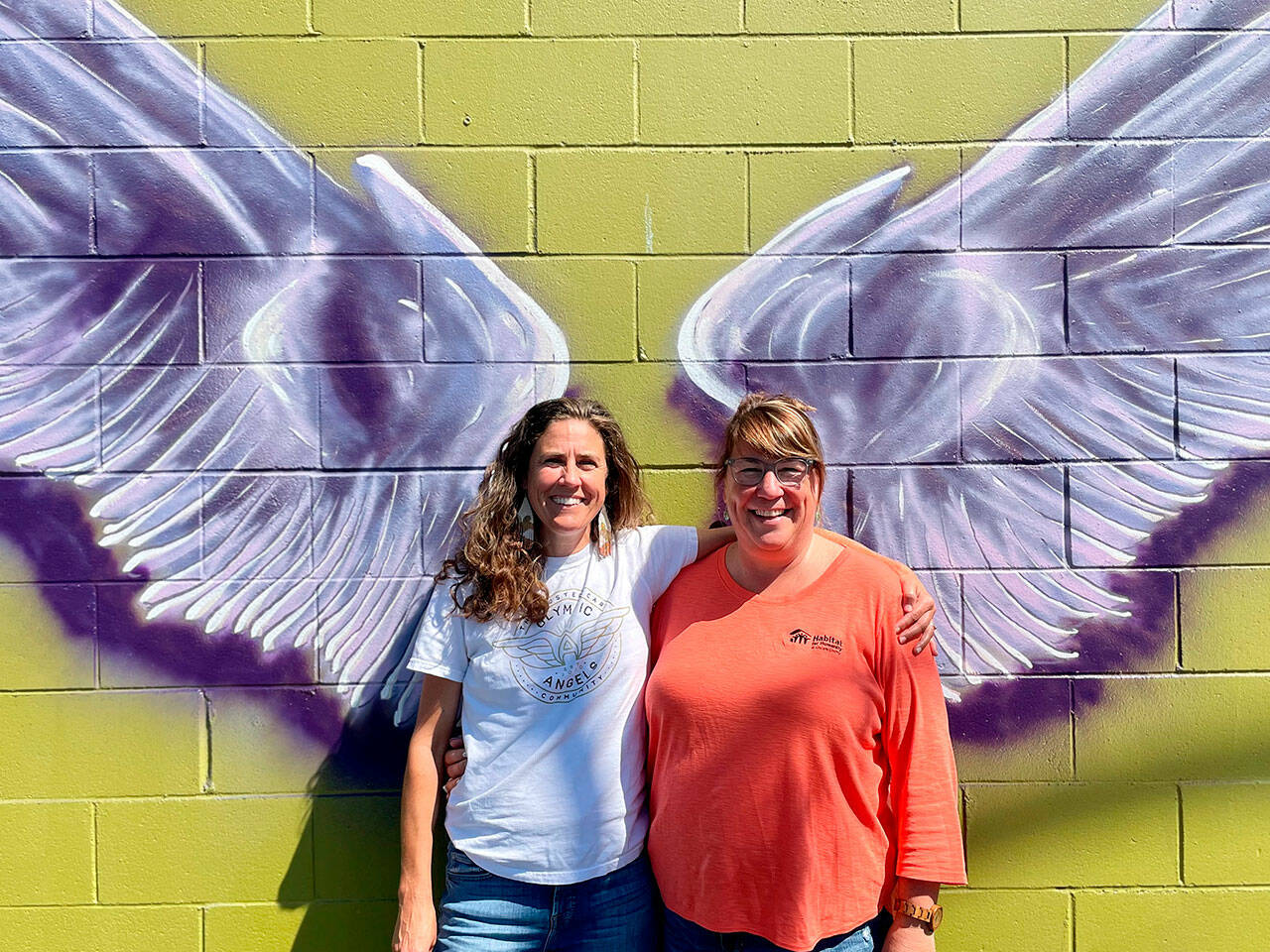 A mural by Craig Robinson in downtown Sequim represents a new partnership between Olympic Angels and Habitat for Humanity of Clallam County. Executive director Morgan Hanna with Olympic Angels, left, said they seek volunteers and mentors to help foster families. Colleen Robinson, chief executive officer for Habitat, said people are welcome to take photos on the wall of Habitat’s Boutique Store and they’ll place a sandwich board sign with information outside, and provide pamphlets about Olympic Angels during business hours. (Matthew Nash/Olympic Peninsula News Group)