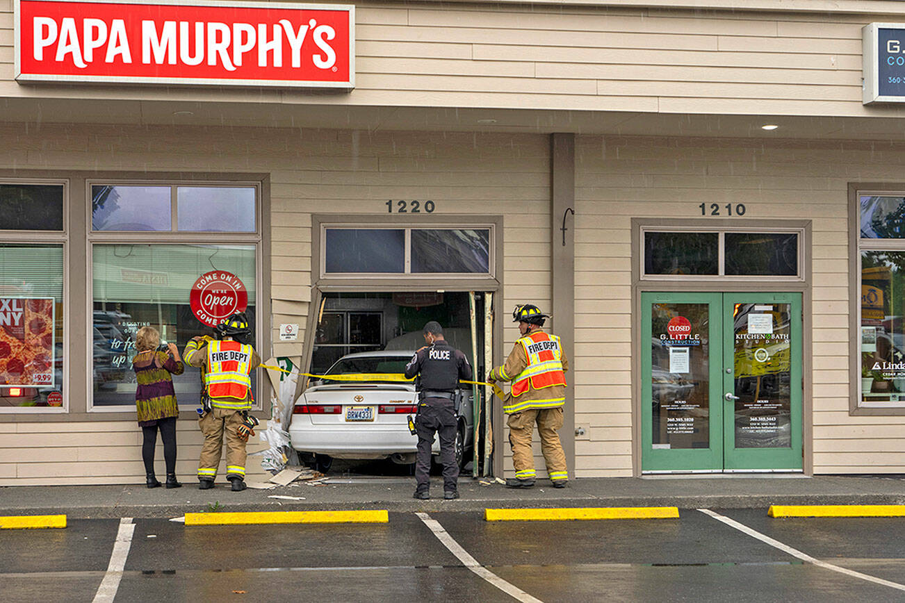 Personnel from East Jefferson Fire and Rescue (EJFR) and Port Townsend police investigate the scene where a Toyota driven by a Quilcene woman crashed into the doorway of Papa Murphy’s pizza shop at 1220 W. Sims Way in Port Townsend before noon on Tuesday. She was not injured, but she was shaken up by the incident that occurred when her foot slipped off the brake pedal and hit the accelerator, according to EJFR Chief Bret Black. (Steve Mullensky/for Peninsula Daily News)