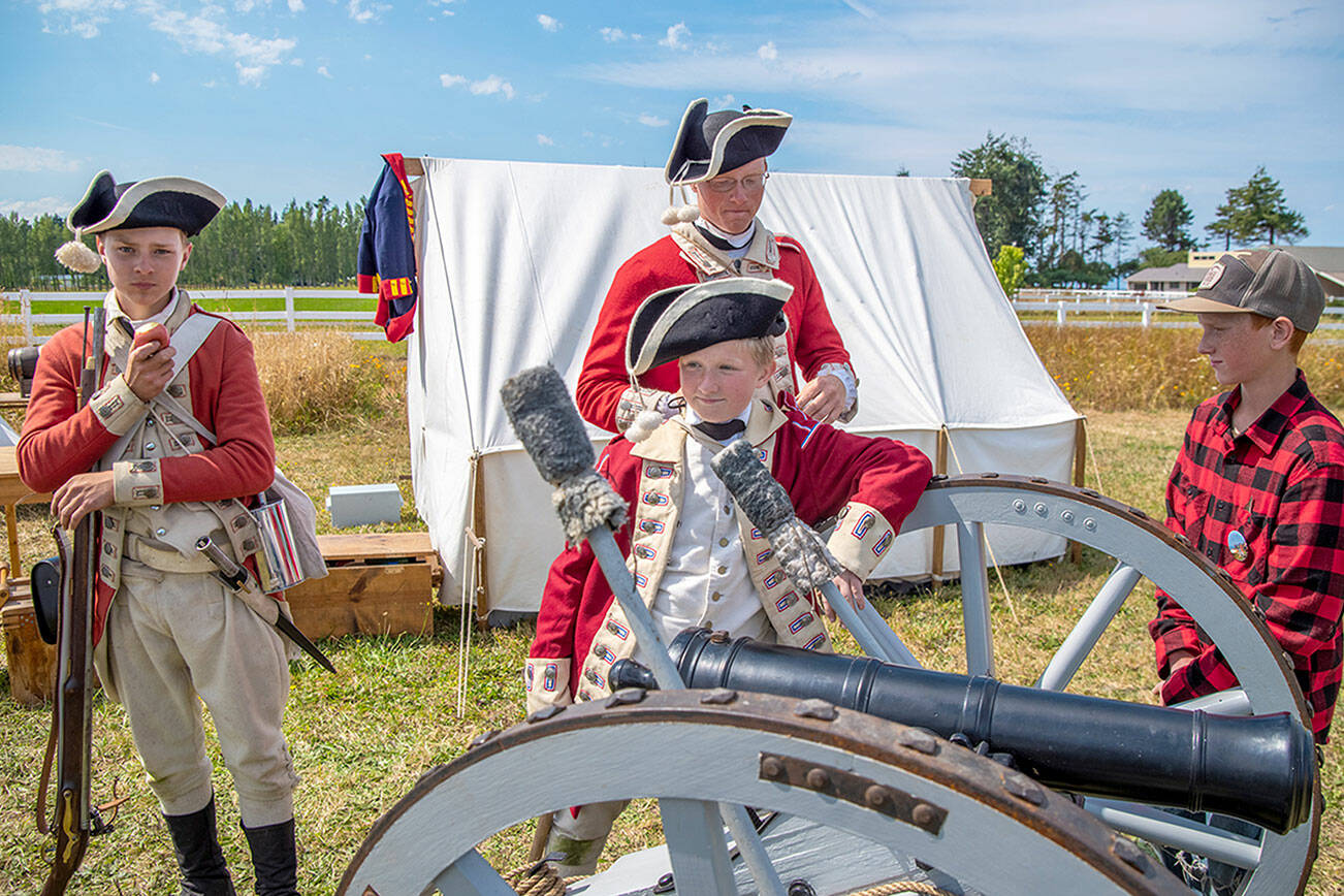 Dressed as British soldiers at the time of the American Revolution, Peter Berneking of Sequim, Thomas House-Higgins of Olympia and Luke Berneking explain about how a three pound ball fits into this particular cannon while Caleb Berneking looks on.