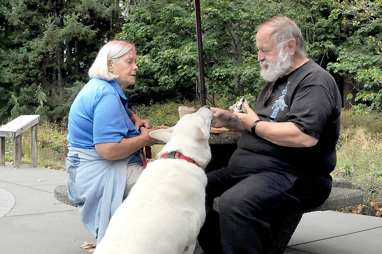 KEITH THORPE/PENINSULA DAILY NEWS
Lin Norris, left, watches as her husband, George Norris, feeds a tidbit to their rescued German sherpard, Storm King, on the patio of the Dungeness River Nature Center in Sequim. The trio were on an outing to Railroad Bridge Park with a stop for coffee and snacks at the center.