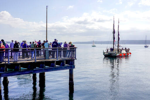 People line the dock at the Northwest Maritime Center to greet the Polynesian Voyaging Canoe, Hōkūleʻa, as it prepares to dock in Port Townsend after it was towed from Tacoma early Tuesday. The Hawaii-based Hōkūleʻa began its journey in Juneau, Alaska, and will visit 36 countries and nearly 100 indigenous territories before reaching its final destination in Japan. (Steve Mullensky/for Peninsula Daily News)