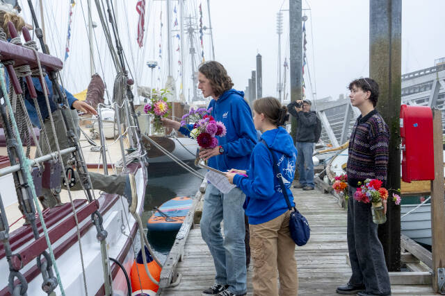 Steve Mullensky/for Peninsula Daily News
Ocean Smith gets ready to hand off a vase of flowers to a Northwest Maritime Center sailing team member already aboard during an early Friday morning delivery of flowers purchased on Thursday. Looking on are teammates Ava Butterfield and Charley Capel.