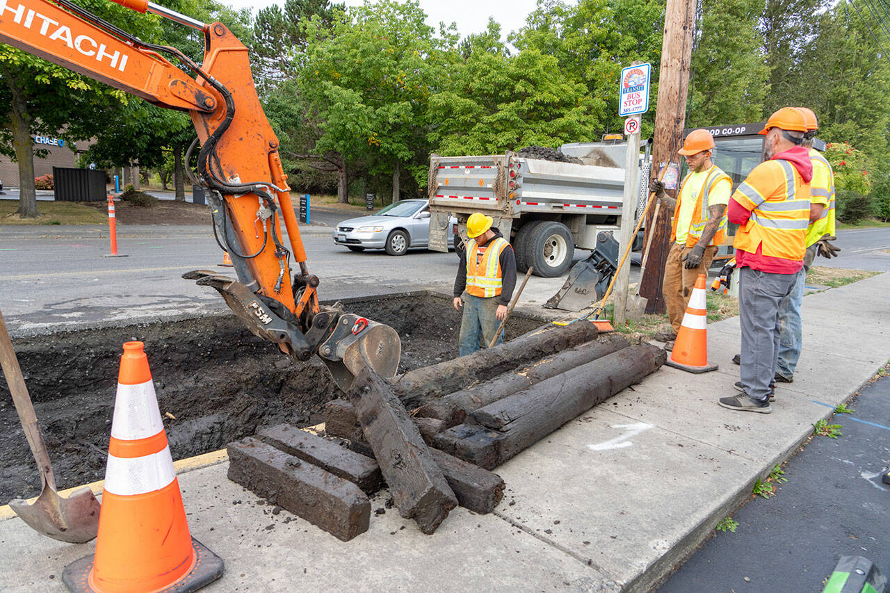 A crew from Port Townsend Public Works watches as a backhoe removes water-logged timber from a sinkhole on Kearney Street outside the Food Co-op on Tuesday at the start of construction of a traffic circle at the intersection of state Highway 20/East Sims Way and Kearney Street in Port Townsend. Traffic heading eastbound toward Port Townsend will detour at Benedict Street and turn left on Washington Street to return to Highway 20/East Sims Way. Traffic going westbound away from Port Townsend will turn right at Kearney Street and left onto Jefferson Street to continue on Highway 20. The detour configuration will last about four weeks, according to the state Department of Transportation. (Steve Mullensky/for Peninsula Daily News)