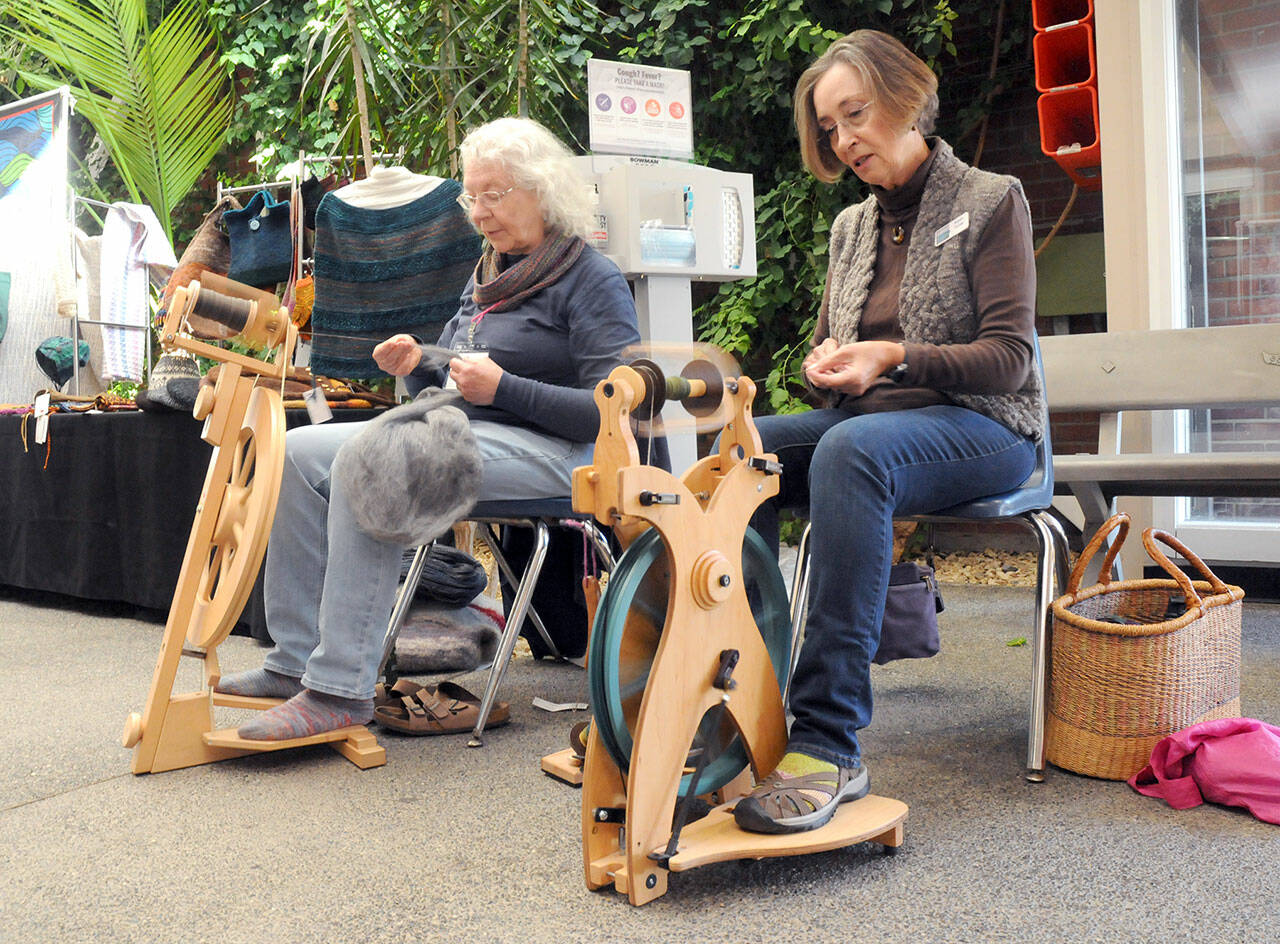 Janice Dotson of Port Angeles, left, and Karen Turner of Sequim, both members of the North Olympic Shuttle & Spindle Guild, pull yarn on spinning wheels as part of a demonstration of the art during the Pacific Northwest Fiber Exposition on Saturday at Vern Burton Community Center in Port Angeles. The three-day expo featured workshops, demonstrations and a marketplace of yarns and fibers. (Keith Thorpe/Peninsula Daily News)