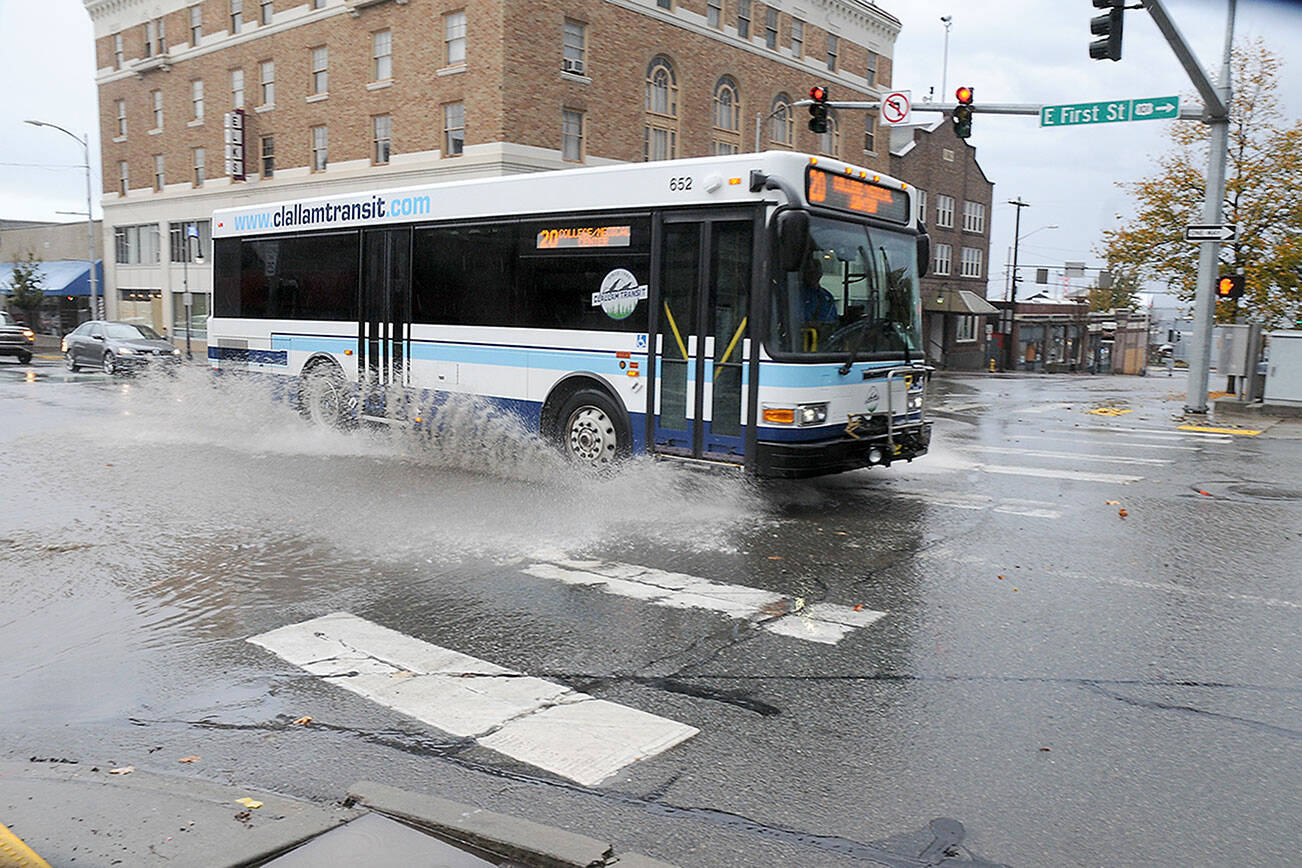 A Clallam Transit bus passes through a flooded intersection at First and Lincoln streets in downtown Port Angeles after heavy rains associated with a passing thunderstorm dropped copious amounts of precipitation over a short period around the area on Monday afternoon. Numerous lightning strikes were recorded during the deluge. (Keith Thorpe/Peninsula Daily News)
