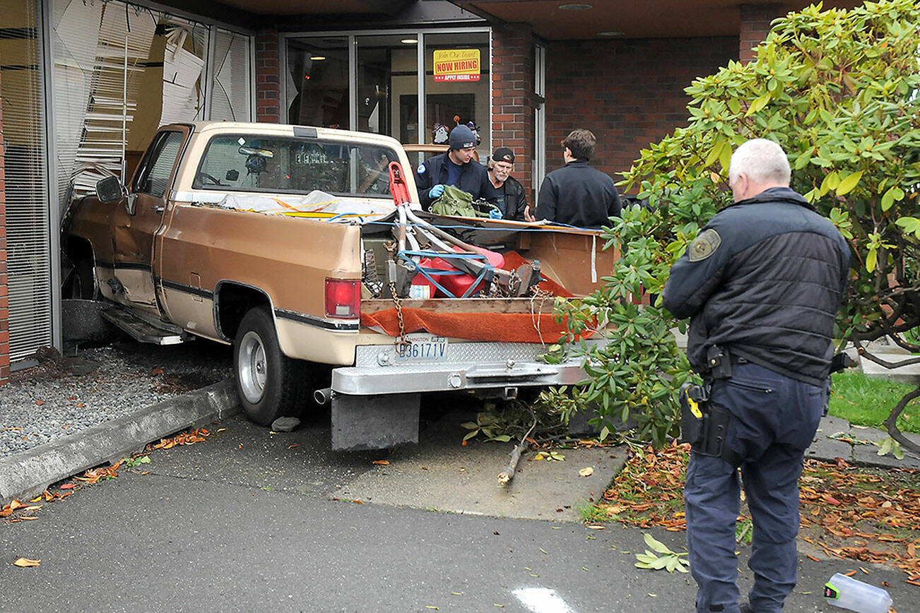 A two-vehicle wreck ended in a pickup driving into Caregivers Home Health at 622 E. Front St. early Tuesday afternoon, according to Port Angeles Police Sgt. Kevin Miller, pictured far right. The pickup, driven by Linda Turman of Port Angeles, was on the far right of the road when it switched to the left lane, which was occupied by a late model Ford Mustang, Miller said. The pickup hit the building. Turman was reported in satisfactory condition at Olympic Medical Center later in the day. The Mustang was damaged but did not crash into anything or block traffic. Turman was cited for improper lane use, Miller said. (Keith Thorpe/Peninsula Daily News)