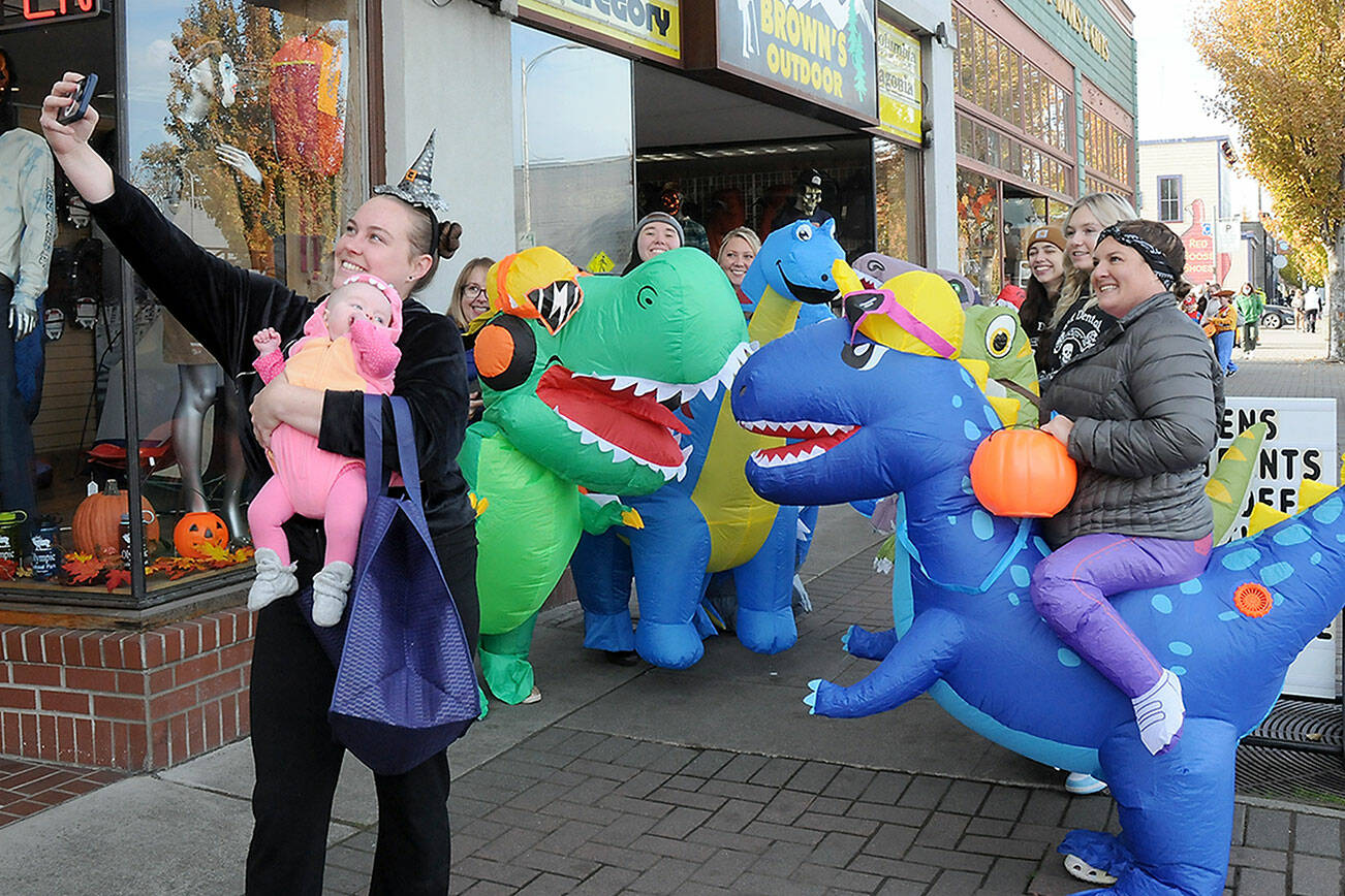 Jessica Jackson of Joyce and her son Blakely Baker, 5 months, pose for a selfie with a herd of inflatable dinosaurs ridden by employees of Port Angeles-based Eleven Eleven Dental during Tuesday’s Halloween trick-or-treating event in downtown Port Angeles. Riders were, from left, Dr. Erin Ostteen, Taylor Peabody, Krystal Feris, Emma Lindberg, Kelly Wheeleer and Alexis Perry. (Keith Thorpe/Peninsula Daily News)