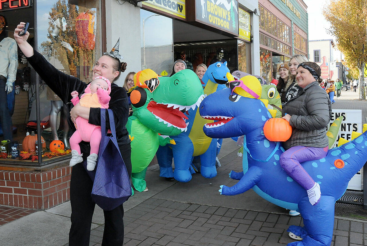 Jessica Jackson of Joyce and her son Blakely Baker, 5 months, pose for a selfie with a herd of inflatable dinosaurs ridden by employees of Port Angeles-based Eleven Eleven Dental during Tuesday’s Halloween trick-or-treating event in downtown Port Angeles. Riders were, from left, Dr. Erin Ostteen, Taylor Peabody, Krystal Feris, Emma Lindberg, Kelly Wheeleer and Alexis Perry. (Keith Thorpe/Peninsula Daily News)