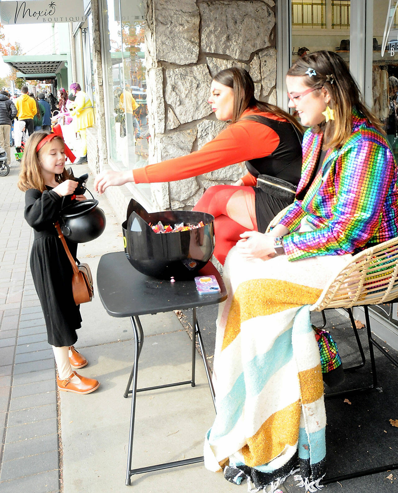 Nimue Garling, 7, of Port Angeles receives a treat from Annie Robertson and Lily Robertson, right, employees of Moxie Boutique, during Tuesday’s Halloween celebration in downtown Port Angeles. (Keith Thorpe/Peninsula Daily News)