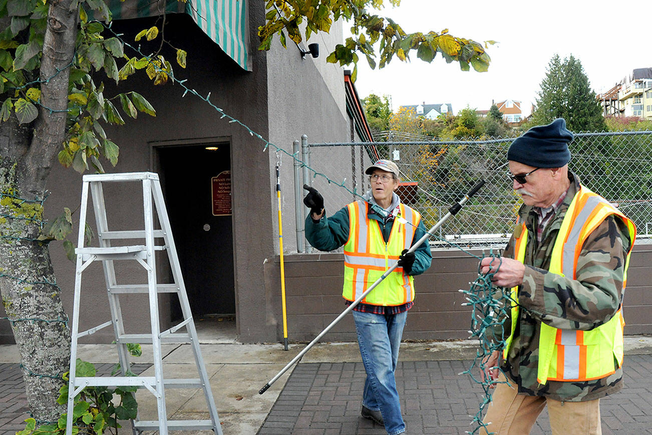KEITH THORPE/PENINSULA DAILY NEWS
Tim Crowley, left, and Frank Bruni, members of the Olympic Kiwanis Club, string Christmas lights on a street-side tree on Friday in downtown Port Angeles. Members of the club take on the annual task of adorning trees and poles in the downtown area with lights with reimbursement from the Port Angeles Downtown Association.